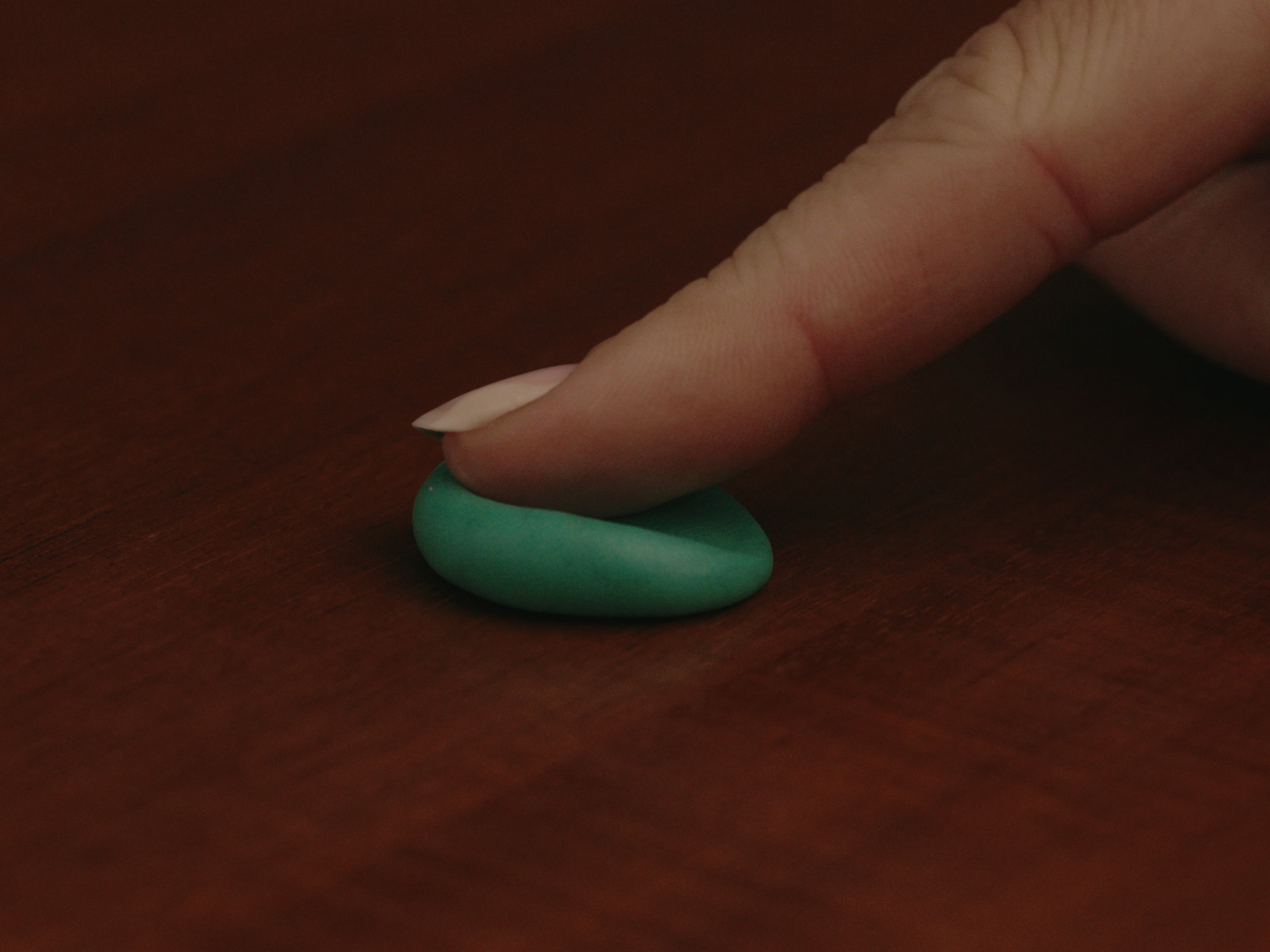 A close-up image of a green dental impression mold resting on a red surface, with a finger partially visible above the mold.