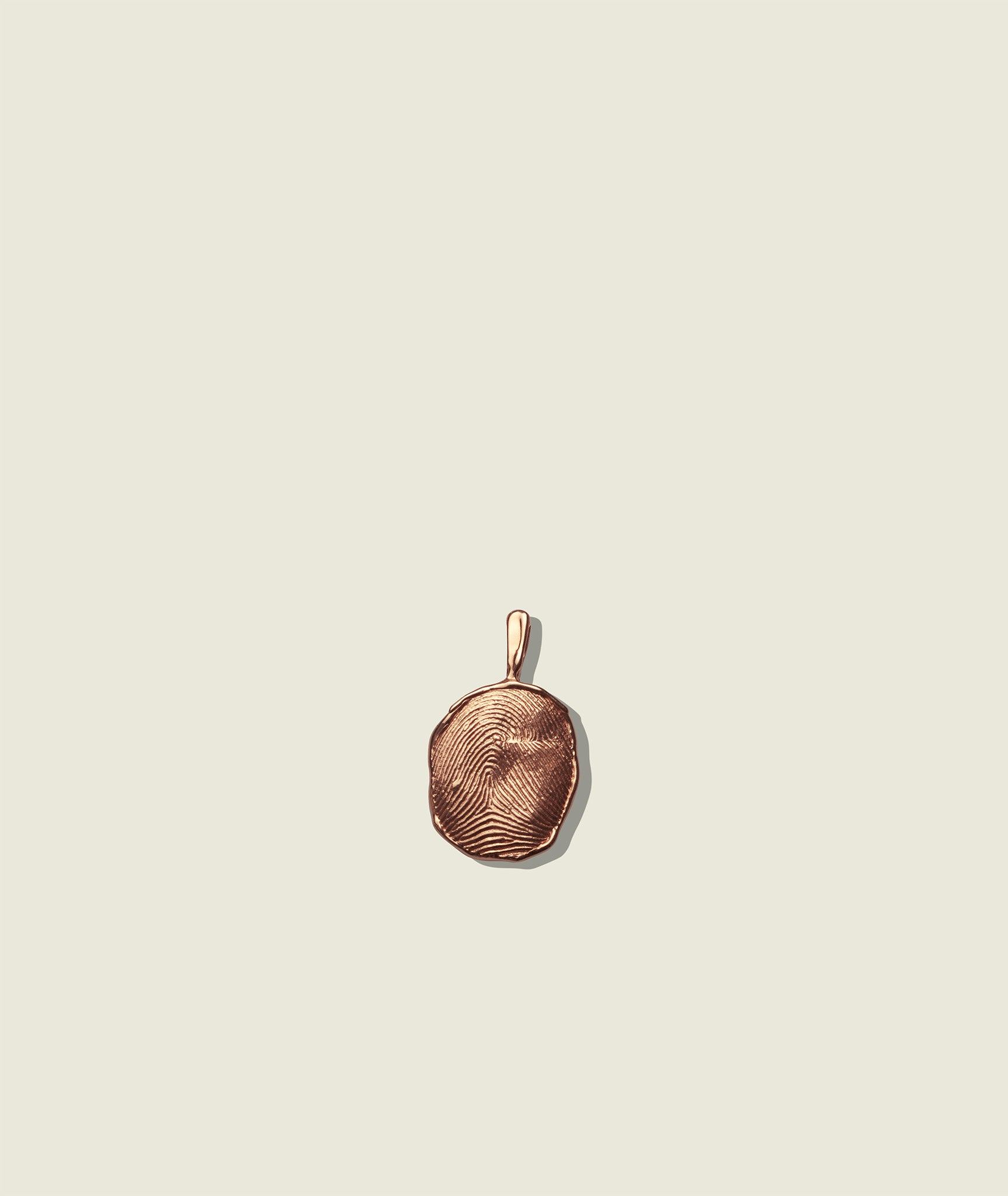 A gold-colored pendant with a fingerprint impression