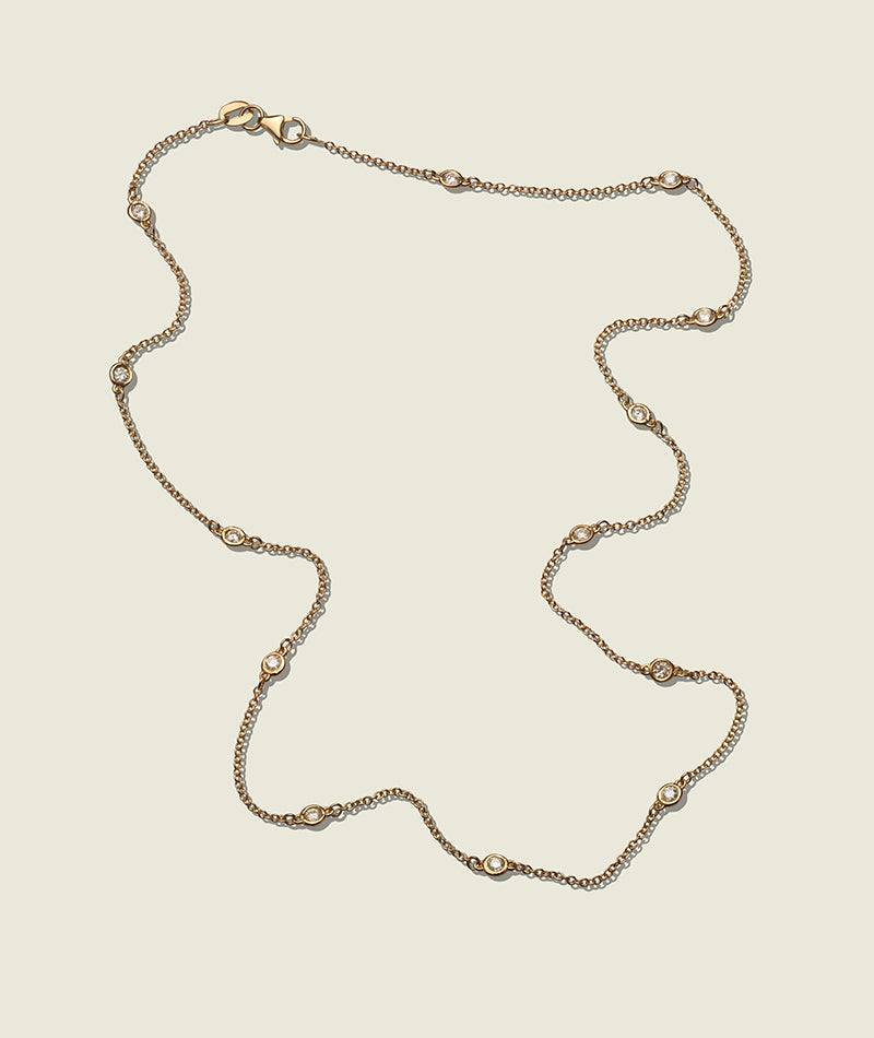 An 18k gold trace chain necklace with a bezel-set round brilliant cut diamond pendant.